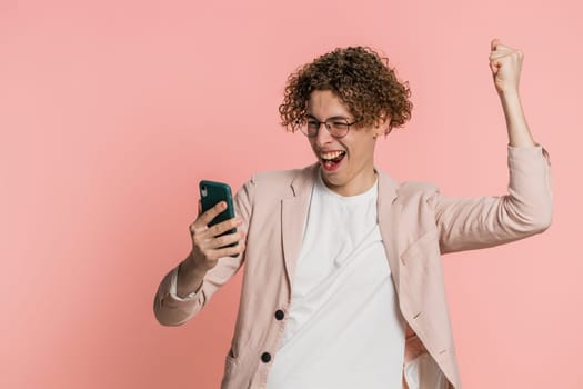 Happy excited Caucasian young man guy use smartphone typing browsing shouting say wow yes found out great big win good news lottery goal achievement celebrating success, winning play game on pink