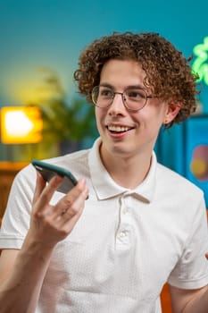 Happy Caucasian man making phone call conversation with friends at modern home room apartment. Young brunette guy enjoying mobile loudspeaker talking gossip, rumors, good news sitting on couch indoors