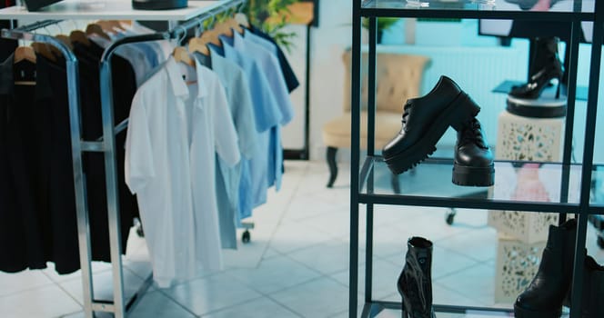 Empty modern clothing store filled with formal wear designs, retail shop with fashion items on hangers and racks. Shopping center boutique with trendy accessories and shoes on display. Camera B.