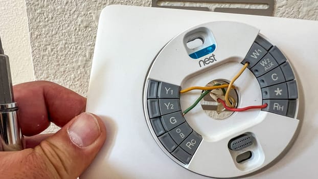 Denver, Colorado, USA-May 18, 2024-Close-up of a Nest thermostat wiring installation, showing various color-coded wires connected to labeled terminals. The image captures the detailed work involved in setting up a smart thermostat.