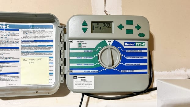 Denver, Colorado, USA-May 27, 2024-A Hunter Pro-C irrigation controller is installed on a garage wall, displaying settings and system controls for efficient lawn and garden watering. The unit is open, revealing the internal programming instructions and interface.