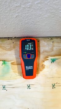 Denver, Colorado, USA-May 19, 2024-A Klein Tools moisture meter is shown measuring the moisture content in a piece of plywood, indicating 30.1 percent. The scene highlights the importance of moisture detection in construction and woodworking.