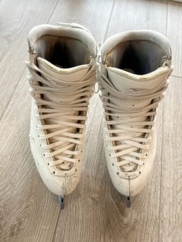 Denver, Colorado, USA-April 20, 2024-A close-up shot of a pair of white ice skates with gold accents, placed on a wooden floor. The skates show signs of use, adding character to the image.