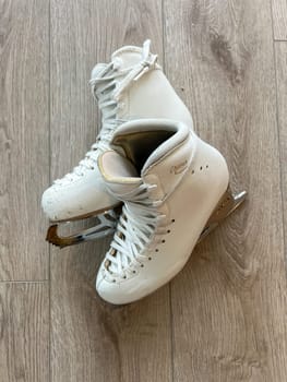 Denver, Colorado, USA-April 20, 2024-A close-up shot of a pair of white ice skates with gold accents, placed on a wooden floor. The skates show signs of use, adding character to the image.