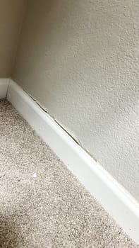 Denver, Colorado, USA-April 29, 2024-Close-up of wall and baseboard damage in a carpeted room, highlighting a significant crack and separation between the wall and trim. The image showcases a common home repair issue.