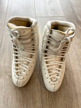 Denver, Colorado, USA-April 20, 2024-A close-up shot of a pair of white ice skates with gold accents, placed on a wooden floor. The skates show signs of use, adding character to the image.