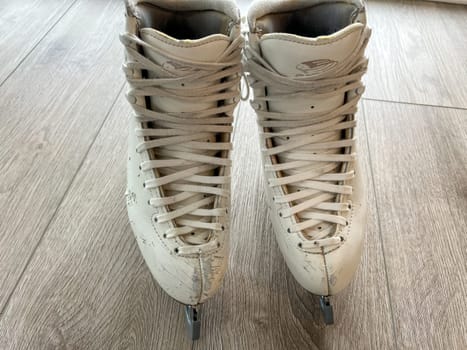 Denver, Colorado, USA-April 20, 2024-A close-up shot of a pair of white ice skates with gold accents, placed on a wooden floor. The skates show signs of use, adding character to the image.