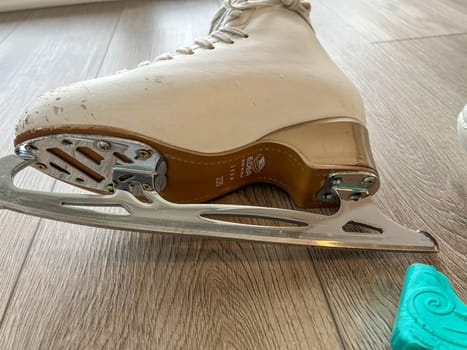 Denver, Colorado, USA-April 20, 2024-A close-up shot of a pair of white ice skates with gold accents, placed on a wooden floor. The skates show signs of use, adding character to the image.