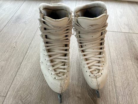 Denver, Colorado, USA-April 20, 2024-A close-up shot of a pair of white ice skates with gold accents, placed on a wooden floor. The skates show signs of use, adding character to the image.