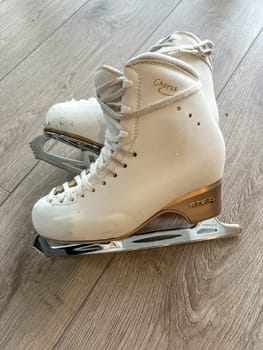 Denver, Colorado, USA-April 20, 2024-A close-up shot of a pair of white ice skates with gold accents, placed on a wooden floor. The skates show signs of use, adding character to the image.