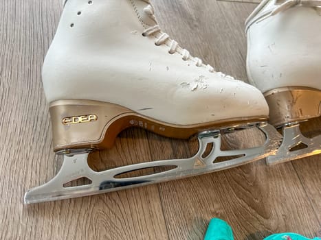 Denver, Colorado, USA-April 20, 2024-A close-up shot of a pair of white ice skates with gold accents, placed on a wooden floor. The skates show signs of use, adding character to the image.