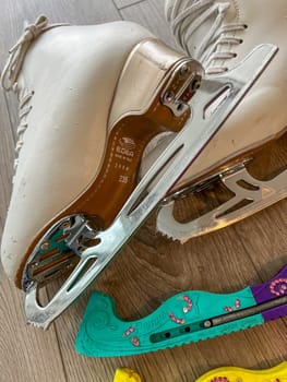Denver, Colorado, USA-April 20, 2024-A close-up shot of a pair of white ice skates with gold accents, placed on a wooden floor. The skates show signs of use, adding character to the image.