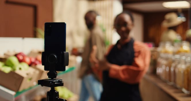 Market employee creating marketing commercial video to attract clients, promoting additives free pantry supplies in reusable jars and locally grown produce. Woman presenting bio products. Camera 2.