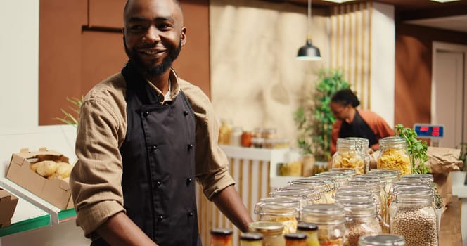 African american farmer opening local zero waste store with natural additives free bulk products and homegrown produce. Merchant preparing goods in reusable jars at eco supermarket. Camera 2.