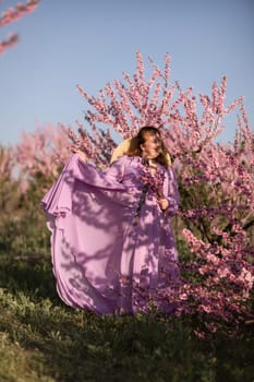 Woman blooming peach orchard. Against the backdrop of a picturesque peach orchard, a woman in a long pink dress and hat enjoys a peaceful walk in the park, surrounded by the beauty of nature