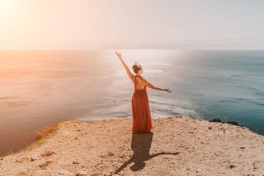 Woman red dress sea. Female dancer in a long red dress posing on a beach with rocks on sunny day. Girl on the nature on blue sky background