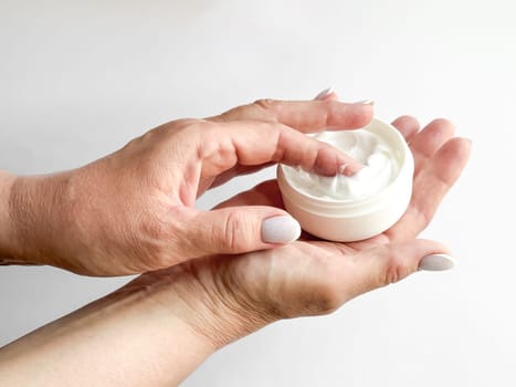 Close up of middle age woman hands holding container of cream and dipping finger on white background. Skincare and moisturizing concept. For healthcare, wellness, and self care poster. High quality