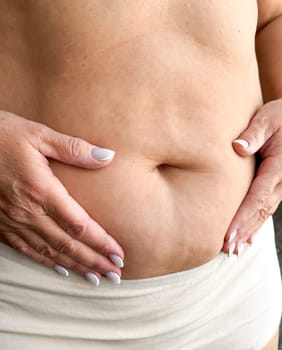 Close up of belly with hands gently touching in beige underwear on white background. Maternity and motherhood concept. Design for healthcare, postpartum care, wellness. High quality photo