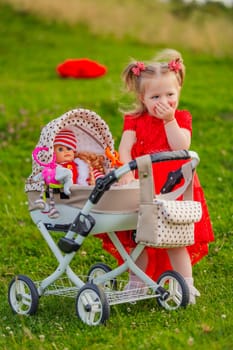 little girl plays with a doll and a stroller on the lawn