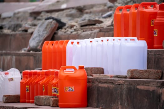 colorful plastic cans in orange saffron and white showing the traditional vessels used to fill holy water from ganga river to take home in India