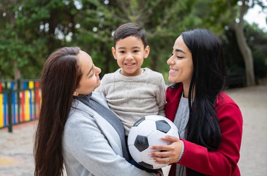 Portrait of latin lesbian couple holding their son with a soccer ball toy. Diversity and LGBT family.