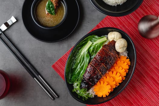 Roast duck with rice and teriyaki sauce on black plate
