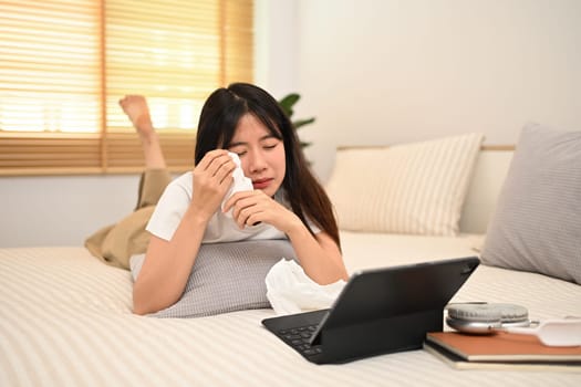 Sad young Asian woman watching dramatic movie and crying on a bed.