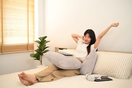 Satisfied young woman stretching arms in bed before remote work at home.