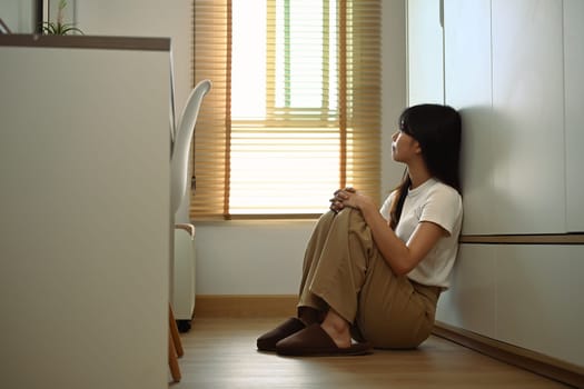 Teenage girl feeling sad sitting on floor and looking away. Psychological and mental health concept.