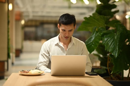 Focused businessman working with laptop during lunch time at cafeteria.