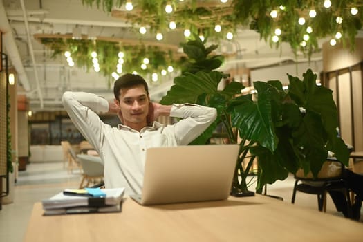 Satisfied businessman taking a break from computer work relaxing at table in office lounge.