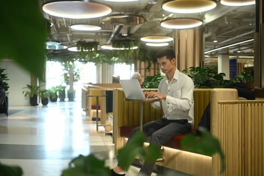 Millennial businessmen using laptop at a table in the lounge area of modern office.