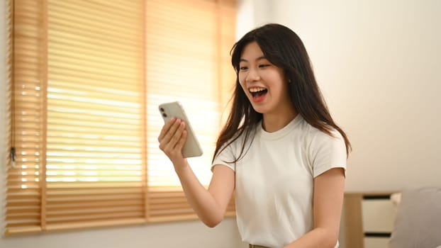 Pretty Asian woman looking at smartphone screen feeling surprise and excitedly.