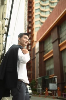 Portrait of confident businessman with coat on the shoulder walking on streets.