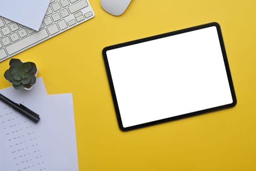 Digital tablet on yellow background with keyboard and potted plant.