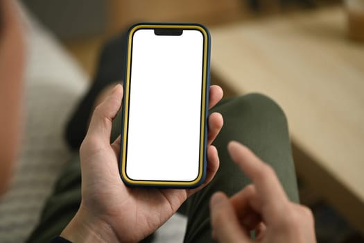 Young man lying on sofa holding smartphone with blank empty screen.