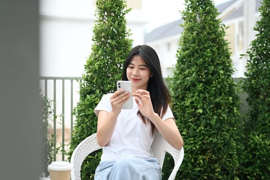 Attractive young asian woman using mobile phone relaxing in the garden surrounded by plants.