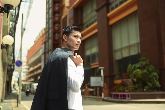 Handsome businessman walking in an urban street with jacket on shoulder.