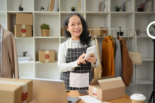 Senior woman small business owner in apron preparing goods for delivery to customer. SME business online concept.