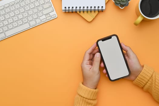 Top view woman holding a smart phone white screen on orange background.