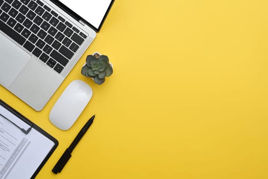 Laptop, financial reports and potted plant on yellow background. Top view with copy space.