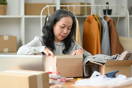 Mature woman packing boxes for delivery at her shop. Business online and e-commerce concept.