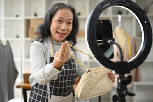 Senior female small business owner showing clothes and present detail during live streaming at her clothing store.