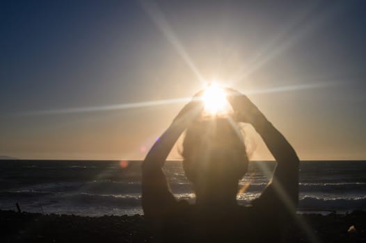 Silhouette of a woman holding the sun in the palm of her hand.