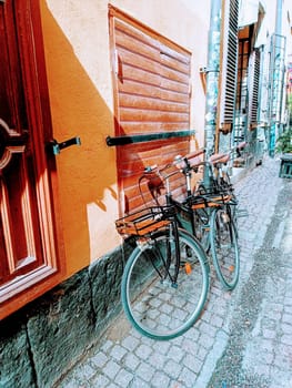 Two black city bicycles with basket staying parked near the orange wall. High quality photo. Vertical mobile photo. City walk, tourism