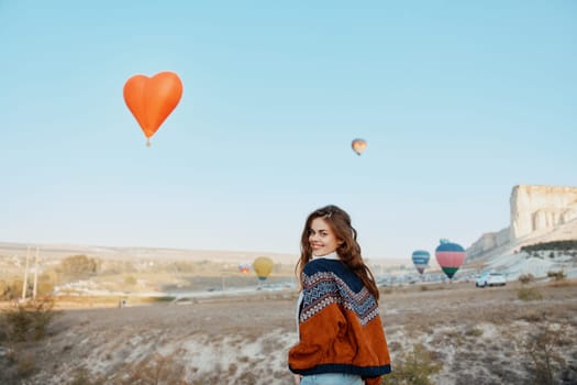 Woman standing in front of heartshaped balloon in sky with other hot air balloons in background