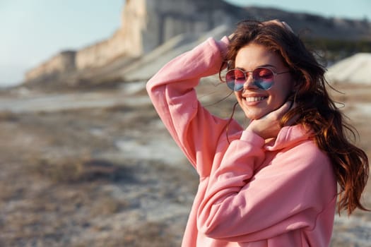 Serene woman in pink sweatshirt and sunglasses enjoying the view of a mountain from the beach