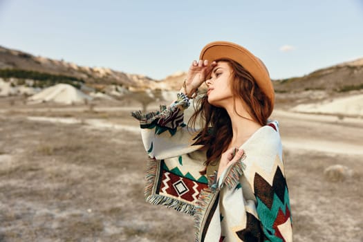 Serene woman in hat and blanket standing in desert with majestic mountains in background