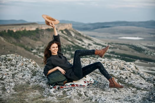 Serene woman relaxing on mountain peak with hat and bag, enjoying tranquil nature view