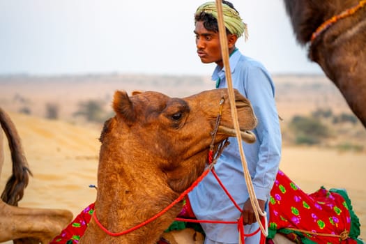 Jaisalmer, Rajasthan, India - 25th Dec 2023: Camel trainer looks on while the camel looks in another direction showing the surprise and confusion on the tourists actions